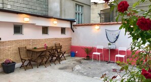 An outdoor patio with a table and chairs, a small garden area with a potted plant, and a red wall with a blue net. - Nomado Hostel (Varna)