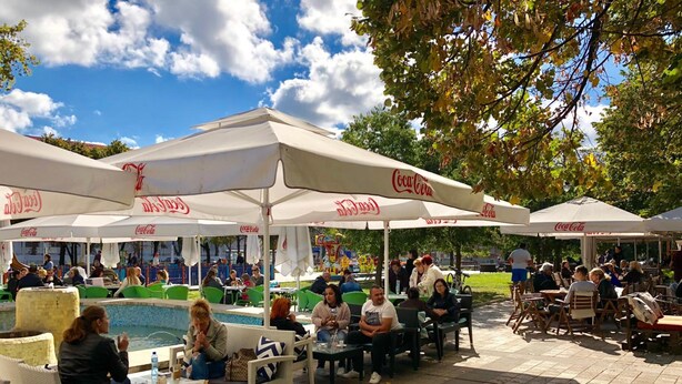 An outdoor seating area with tables and chairs under white umbrellas, a pool, and people dining and socializing. - Nomado Hostel (Varna)