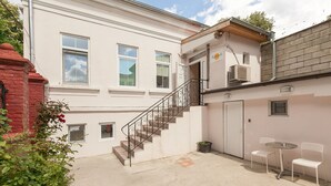 A building with a staircase leading to an upper floor, a small outdoor seating area with chairs and a table, and a door with a sign above it. - Nomado Hostel (Varna)