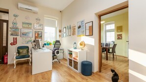 A well-lit office space with a desk, chair, and computer. There are framed pictures on the wall, a small plant, and a cat on the floor. - Nomado Hostel (Varna)