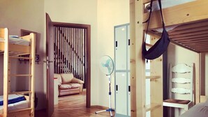 A room with a bunk bed, a sofa, a fan, and a door with lockers. - Nomado Hostel (Varna)