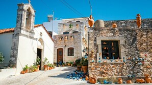 A traditional stone building with a window decorated with pottery, a bell tower, and a paved street with potted plants. - Villa w/Private Pool, Play Area, BBQ & Ping Pong (Rethymnon)