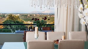 A dining area with a table set for two, a vase with red flowers, and a view of a mountainous landscape. - Villa w/Private Pool, Play Area, BBQ & Ping Pong (Rethymnon)