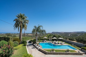 Una piscina con sillas de descanso, palmeras y vistas al paisaje.