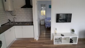Une cuisine compacte avec des meubles blancs, une hotte noire et un évier. On aperçoit une petite console blanche sur laquelle sont posés une plante et un vase.