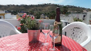 Une table recouverte d’une nappe à pois rouges, avec deux verres à vin, une bouteille de vin et une plante en pot aux fleurs roses.