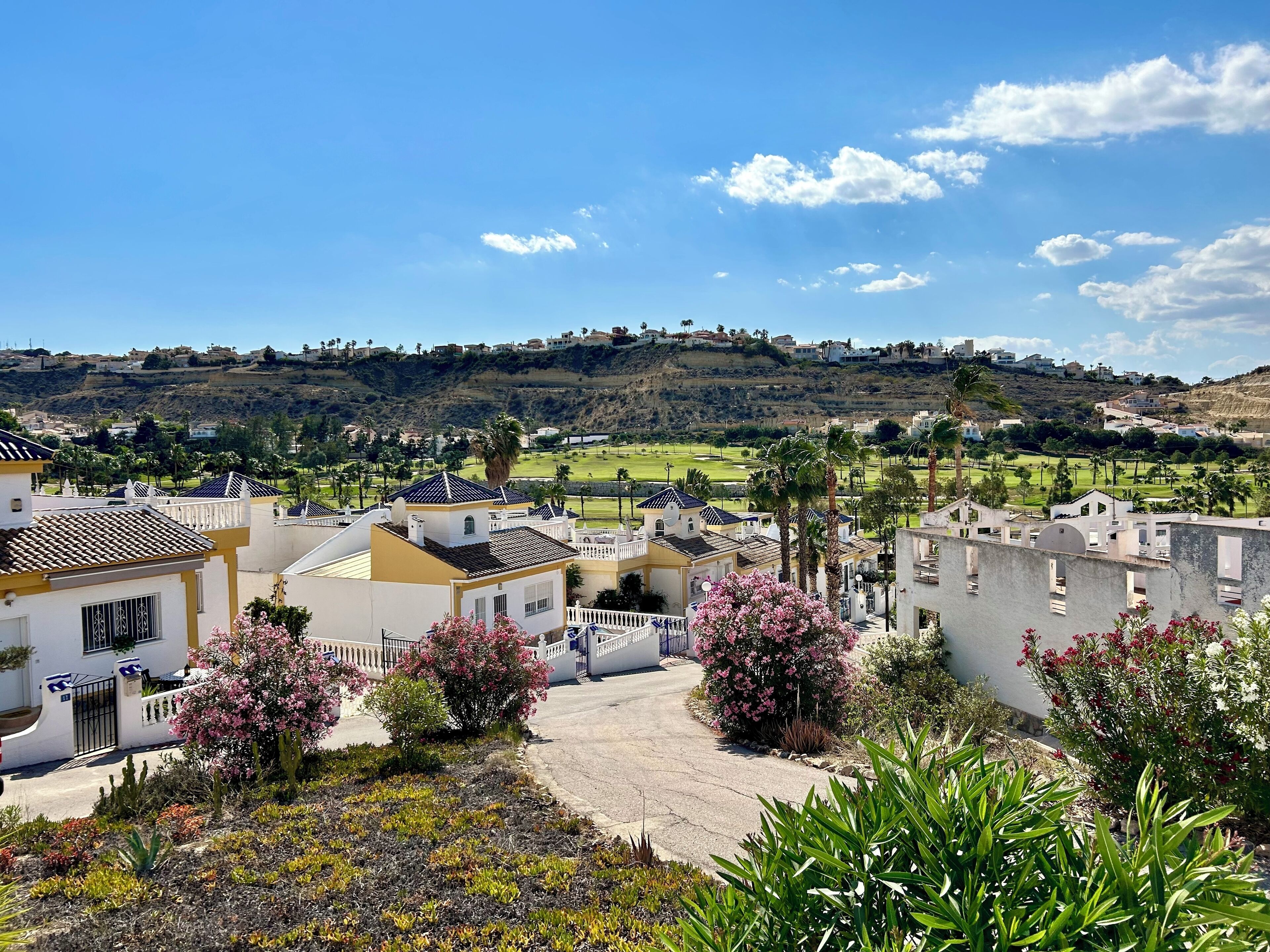 A residential area with houses, a golf course, and a hilly landscape in the background.
