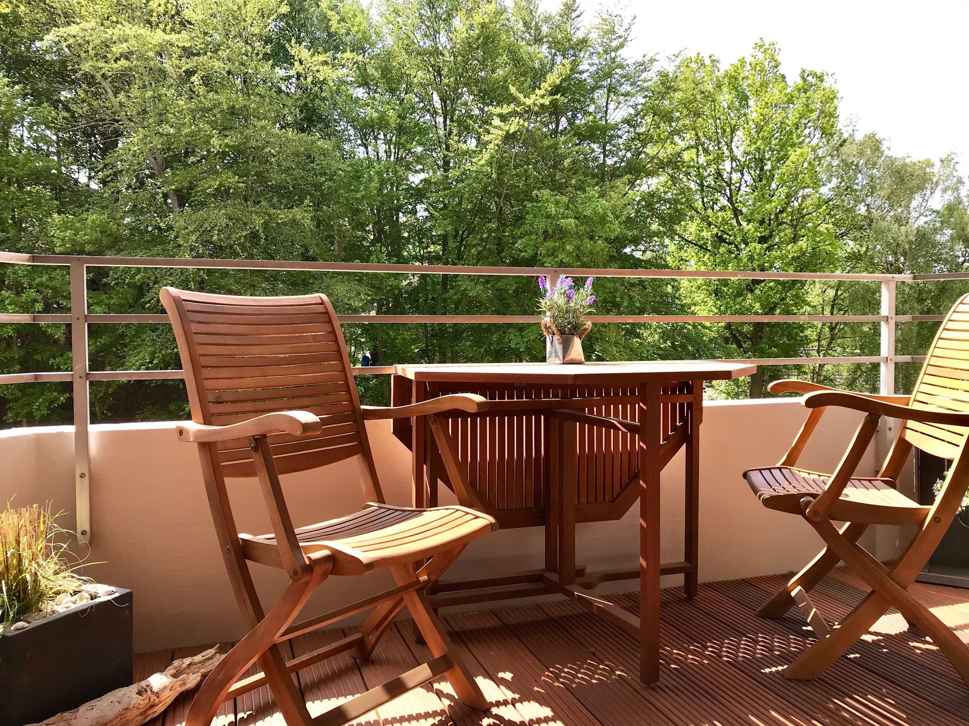 Een houten terras met twee stoelen en een tafel, omringd door een metalen reling.