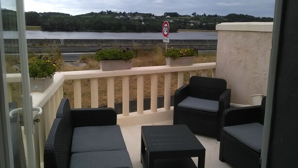 Een balkon met rieten meubilair en plantenbakken, met uitzicht op een rivier en een stad.