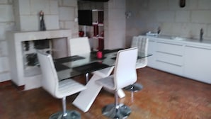 Een eetruimte met een glazen tafel, witte stoelen, een wit kastje en een bakstenen muur.