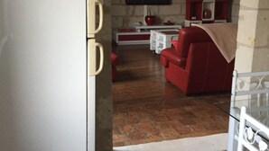 Een ruimtelijke woonruimte met een kitchenette, een rode bank en een witte koelkast.