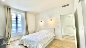 Une chambre à coucher avec un lit, une table de chevet, une fenêtre avec des rideaux, une porte et un luminaire fixé au mur.