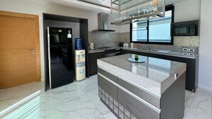 Een moderne keuken met een centraal eiland, inbouwapparatuur en een groot raam boven de spoelbak.