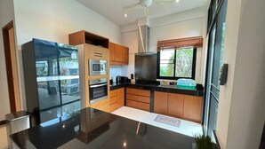 Een moderne keuken met een zwart aanrecht, houten kastjes, roestvrijstalen apparatuur en een plafondventilator.