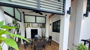 Een terras buiten met een tafel, stoelen, een plafondventilator en potplanten.