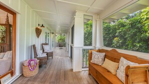 Een overdekt terras met rieten meubels, een houten bank en uitzicht op weelderige begroeiing.