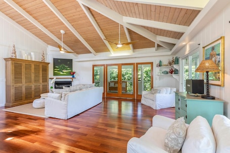 A spacious living room with a wooden ceiling, white sofas, a fireplace, and a large painting.