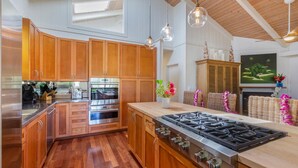 Een moderne keuken met houten kastjes, roestvrijstalen apparatuur en een groot kookeiland met gasfornuis.