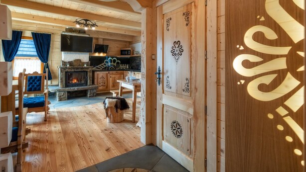 A wooden interior with a stone fireplace, a dining area, and a kitchen with a microwave. - Domki Ze Hej z kominkiem lub sauną (Zakopane)