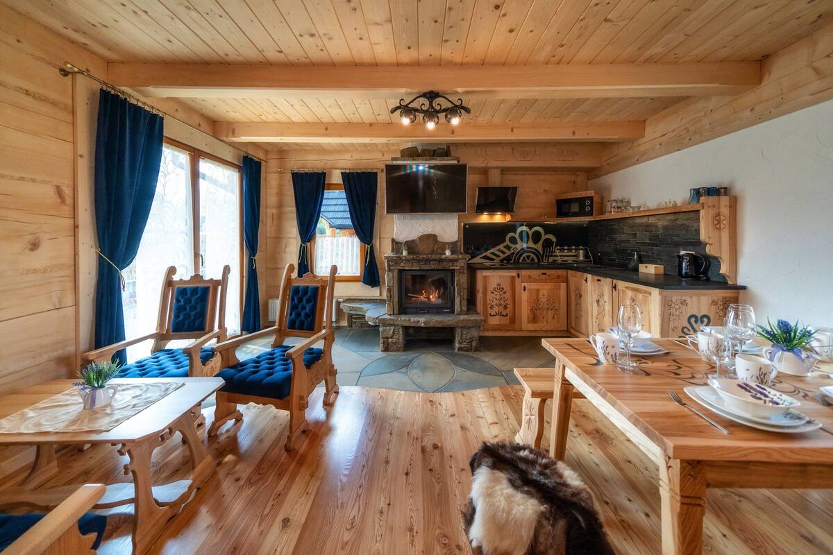 A wooden cabin interior with a dining area, kitchen, and fireplace.