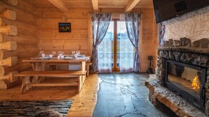 A log cabin interior with a stone fireplace, wooden dining table, benches, and a view through a glass door. - Domki Ze Hej z kominkiem lub sauną (Zakopane)
