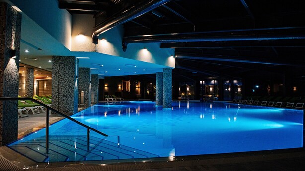 An indoor swimming pool with clear water, surrounded by stone pillars and a staircase leading down. - Hot Springs Medical and Spa Hotel (Razlog)