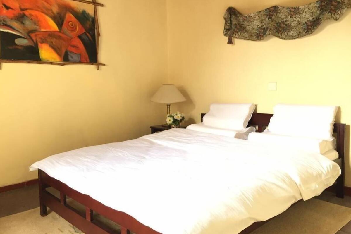 Una cama bien tendida con sábanas blancas en una habitación con una pared amarilla lisa.
