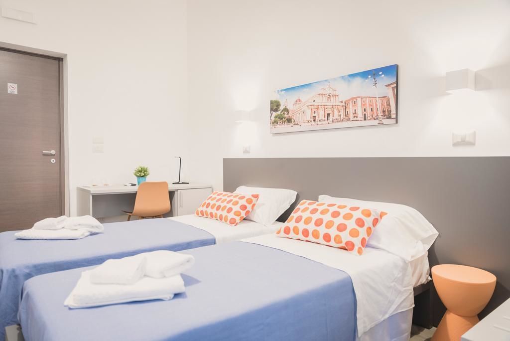 Habitación de hotel con dos camas, un escritorio, una silla y una planta pequeña en maceta.
