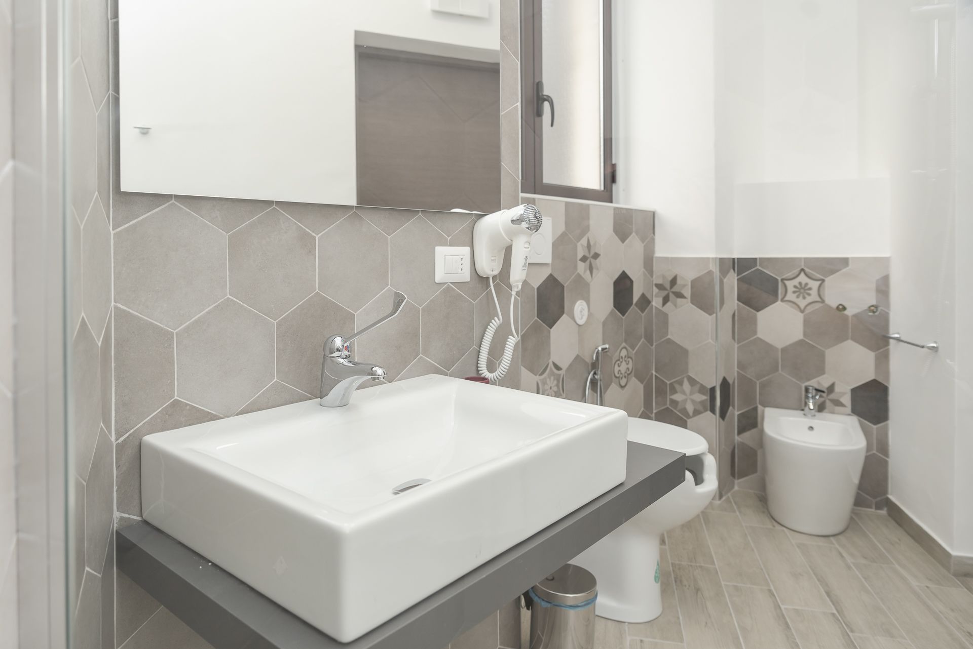 A modern bathroom with a large white sink, a handheld hair dryer, and a toilet.