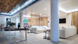 A spacious living area with a modern design, featuring a wooden ceiling, white sofas, and a large table. - Mikelina Boutique Hotel (Pallini)