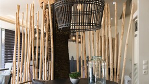 A modern dining area with a round table, two chairs, and a unique wall decoration made of wooden sticks and a woven basket. - Mikelina Boutique Hotel (Pallini)