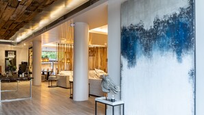 A spacious hotel lobby with a modern design, featuring a large abstract painting, a sculpture, and a seating area with a view of greenery outside. - Mikelina Boutique Hotel (Pallini)