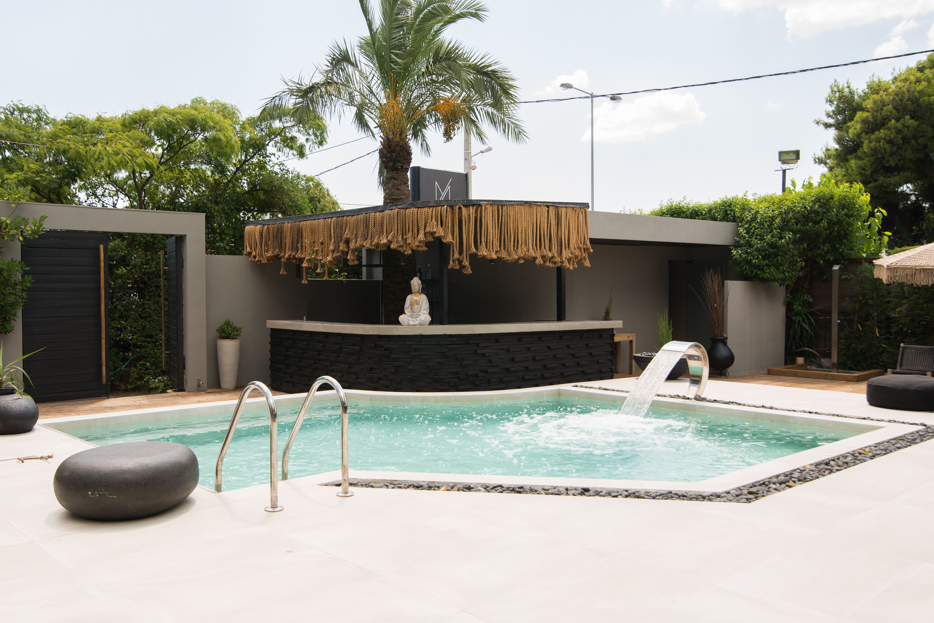 A modern outdoor pool area with a stone wall, a palm tree, and a water feature.