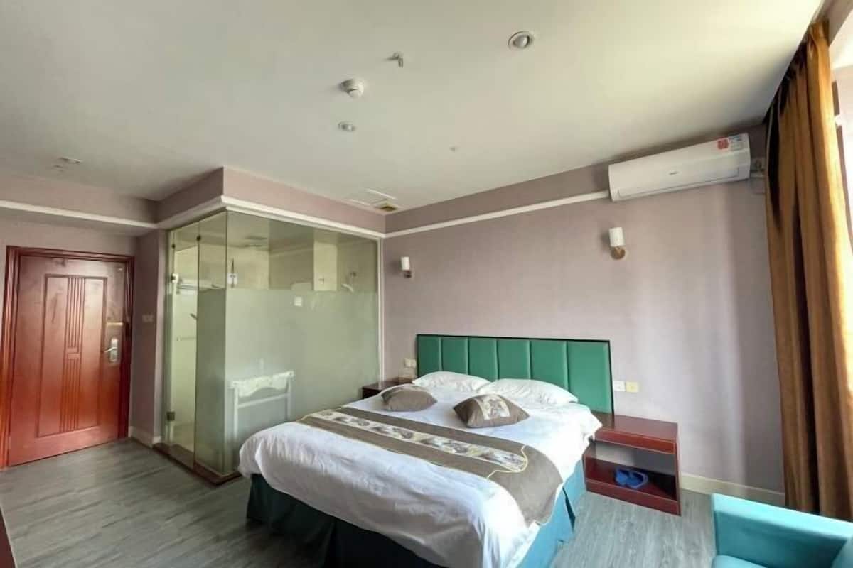 Hotelkamer met een bed, een glazen douchecabine, een houten deur en een klein tafeltje met een stoel.