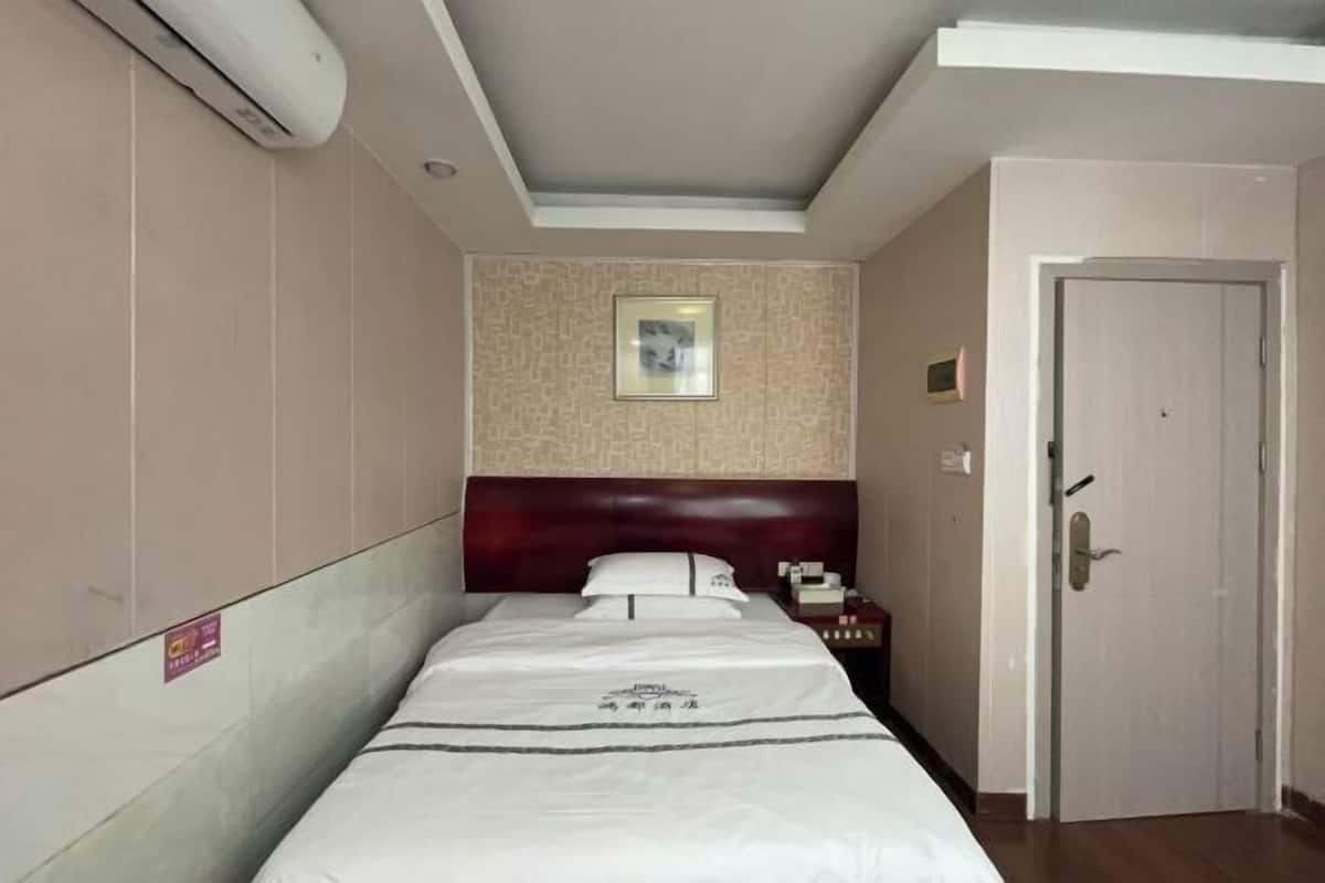Een hotelkamer met een bed, nachtkastje, deur en een luchtverkoeler aan de muur.