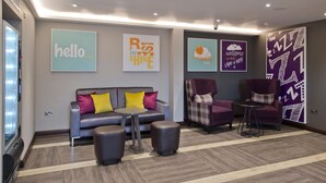A modern lounge area with a sofa, ottomans, and two armchairs, a small round table, and wall art. - Premier Inn Cockermouth (Cockermouth)