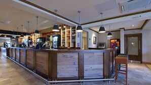 A bar area with a wooden counter, hanging pendant lights, and a sign indicating the direction to toilets. - Premier Inn Cockermouth (Cockermouth)