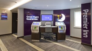 A check-in area with a desk, a monitor, and two self-service kiosks at Premier Inn. - Premier Inn Cockermouth (Cockermouth)