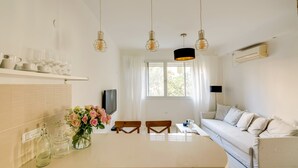 A modern kitchen with a central island, white cabinetry, and a dining area with a white sofa and two wooden chairs. - Double O apartment - Near the bech (Tel Aviv)
