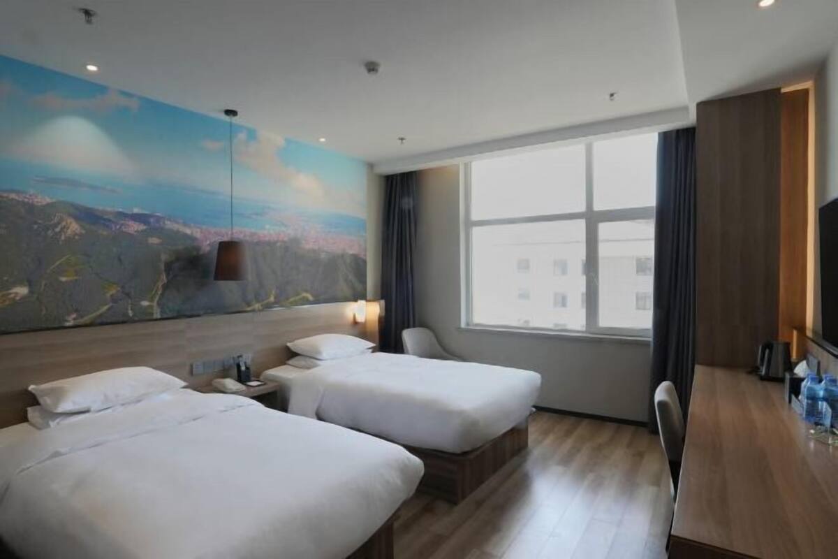 Une chambre d’hôtel avec deux lits, un bureau, une grande fenêtre et une fresque murale.