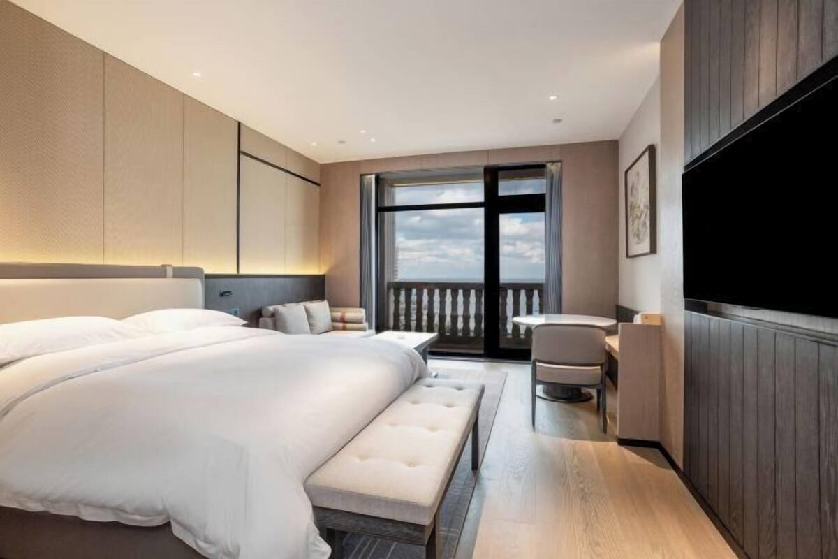 Une chambre d’hôtel moderne dotée d’un grand lit, d’un coin salon, d’une télévision et d’un balcon avec vue.