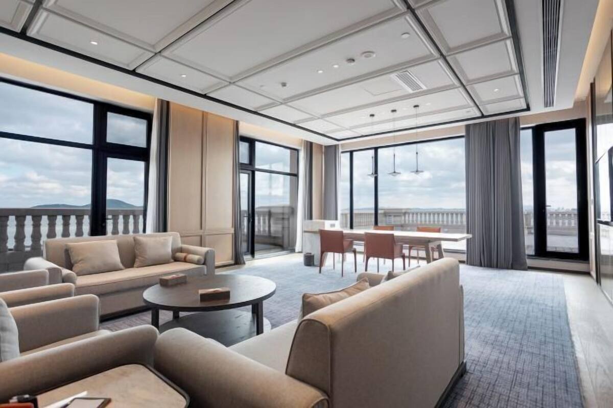 Une chambre d’hôtel moderne dotée d’une grande fenêtre, d’un canapé, d’une table ronde et d’un balcon avec vue.