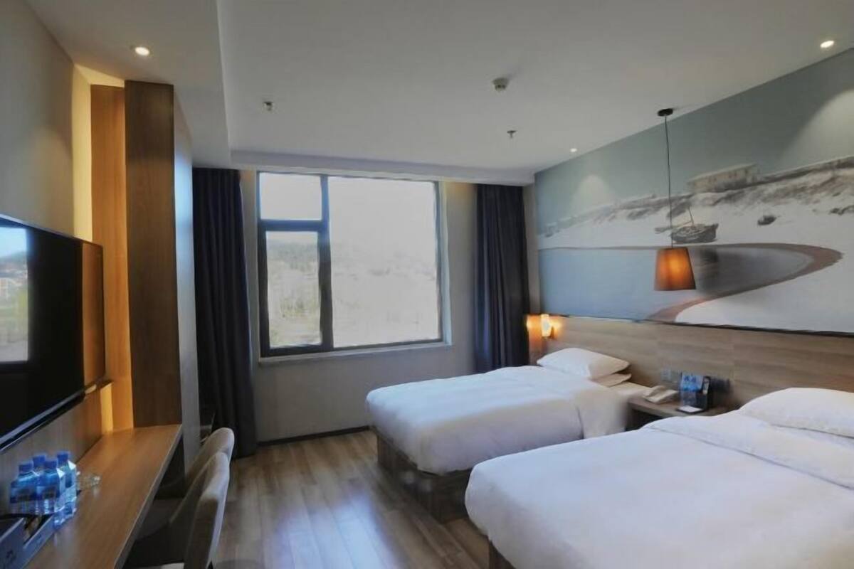 Une chambre d’hôtel avec deux lits, une télévision, un bureau et une grande fenêtre.