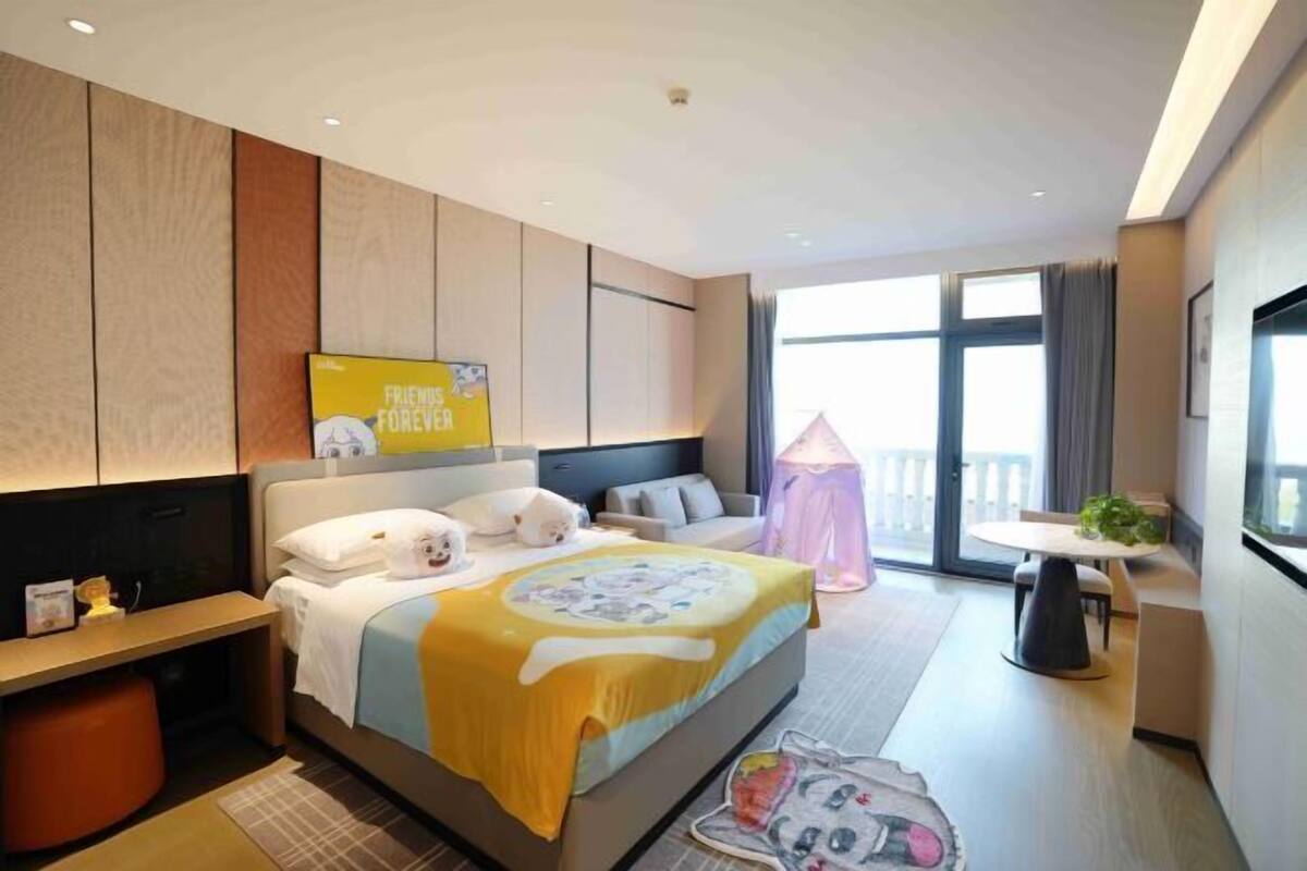 Une chambre d’hôtel moderne dotée d’un grand lit, d’une table de chevet, d’un petit bureau, d’une chaise, d’un balcon avec vue et d’une grande fenêtre.