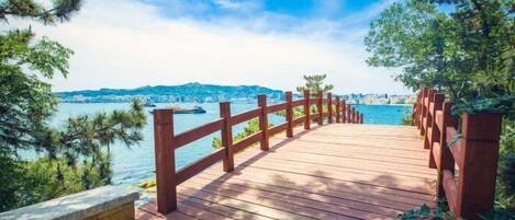 A wooden deck with a red railing overlooking a body of water and distant cityscape.