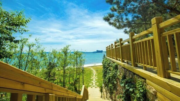 A wooden pathway leading to a beach with a clear view of the sea and distant cityscape. - Weihai Dongshan Hotel (Weihai)