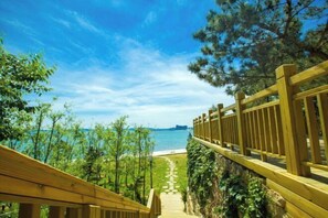 A wooden pathway leading to a beach with a clear view of the sea and distant cityscape. - Weihai Dongshan Hotel (Weihai)