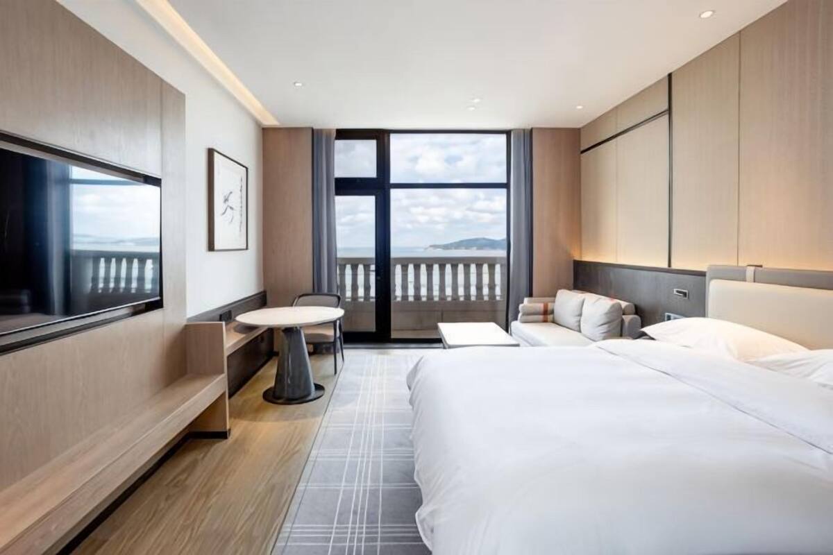 Une chambre d’hôtel équipée d’un lit, d’un bureau, d’une chaise, d’une télévision et d’un balcon avec vue.