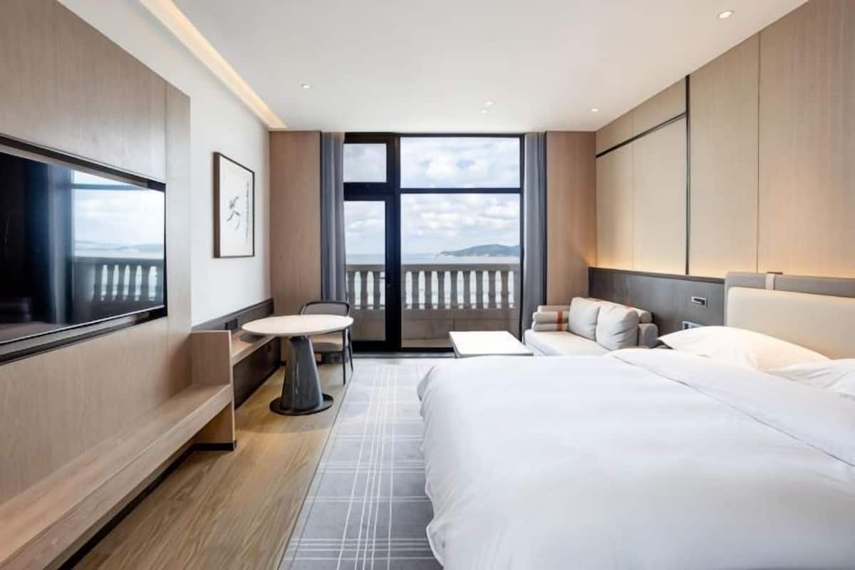 Ein Hotelzimmer mit Bett, Schreibtisch, Stuhl, Fernseher und einem Balkon mit Blick.