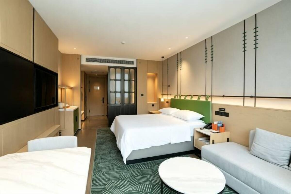 Une chambre d’hôtel avec deux lits, un canapé, une table ronde, une télévision et un miroir.